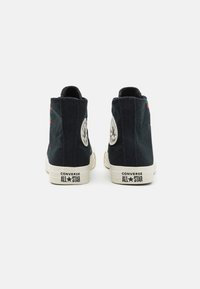 Sneaker alte in tela nera con suole in gomma bianca, caratterizzate da una toppa con logo circolare e ricami colorati sul tallone.