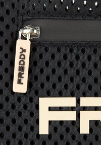Bolsa de malla negra con un bolsillo con cremallera prominente, tirador de plástico con la etiqueta "FREDDY" y grandes letras beis.