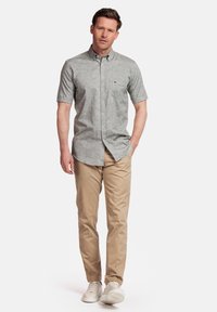 Grijs overhemd met korte mouwen en een textuurafwerking, gecombineerd met beige chino's en witte sneakers, staand tegen een effen achtergrond.