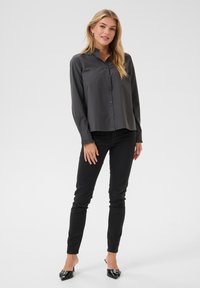 Grijze knoopshirt met lange mouwen en elastische ruches bij de mouwen, gedragen met zwarte skinny jeans en open-toe zwarte hakken, minimalistisch ontwerp.