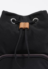 Czarny plecak z zamknięciem na sznurek, wyposażony w zamek z beżowej skóry oraz metalowe oczka na teksturowanej powierzchni materiału.