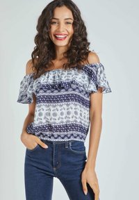 Top sin mangas en blanco y azul marino, con mangas acampanadas y patrones geométricos. Combinado con jeans oscuros de corte ajustado.