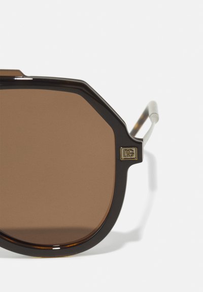 Brown-tinted octagonal sunglasses with a dark tortoiseshell frame and silver metal temples, featuring a gold logo accent on the side.