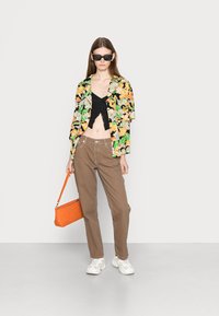 Camisa floral colorida em preto, laranja e verde sobre um top crop preto. Calças castanhas e uma bolsa laranja. Ténis brancos completam o conjunto.