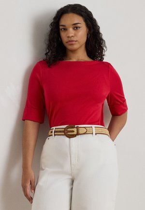 Top roșu cu mâneci scurte și decolteu barcă, textură netedă; asortat cu pantaloni albi cu picioare largi și o curea bej împletită cu o cataramă rotundă.