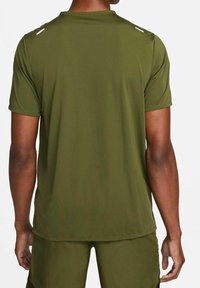 Hombre vistiendo una camiseta de manga corta verde oliva y pantalones cortos a juego, mostrado desde atrás sobre un fondo blanco.