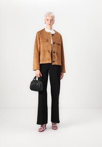 Bruine suède jas met vier zakdetails, zwart gebreid topje, zwarte broek, zwarte handtas en paarse haksandalen.