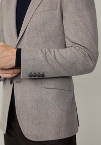 Blazer en laine grise avec une finition texturée, doté d'une poche poitrine unique, de poignets à quatre boutons et d'une coupe ajustée.