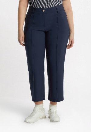 Navy blue cropped pants with a smooth texture, featuring front pockets and a gold button detail at the waist, paired with white sneakers.