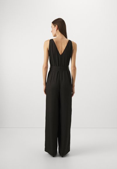 Svart jumpsuit med V-hals, vide ben, beltedetalj i midjen og strukturert stoff, vist fra baksiden på en nøytral bakgrunn.