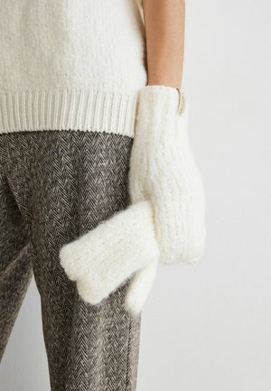 Witte gebreide wanten met een zachte, pluizige textuur en een unieke vorm die op een hand lijkt; gedragen met een patroon van bruine broek.