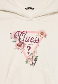 Bijela dukserica s kapuljačom koja ima ružičasti trokutasti grafički dizajn s cvjetnim akcentima i natpisom "Guess Los Angeles" u stiliziranom fontu.