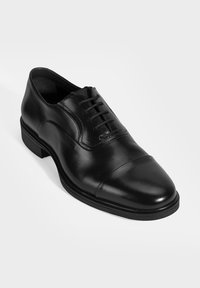 Zwarte leren geklede schoen met een kaptoen, met een vetersluiting en een getextureerde rubberen zool voor grip. Gladde afwerking, gemiddelde hoogte.