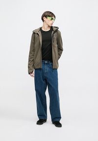 Siva flis jakna s kapuco, črna majica in ohlapne modre džinsu hlače. Zeleno sončna očala in črni čevlji dopolnjujejo opravo.