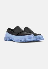 Scarpe slip-on in pelle nera con una ampia suola in gomma blu, caratterizzate da una texture rigata e una finitura liscia nella parte superiore.