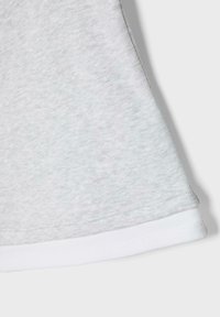 Tissu gris clair avec un détail de couture tressée le long du bord, superposé à un tissu blanc lisse en dessous sur un fond uni.