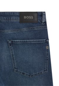 Dark blue denim jeans with a leather BOSS label, featuring a single back pocket and visible stitching details. Zippered pocket accent on the side.