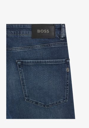 Jeans in denim blu scuro con etichetta in pelle BOSS, dotati di una sola tasca posteriore e dettagli di cucitura visibili. Accento con tasca con zip sul lato.