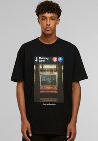 Sort t-shirt med et grafisk motiv af en subway døråbning. Teksten inkluderer "Memory Lane" og retningssymboler i hvide og farvede cirkler.