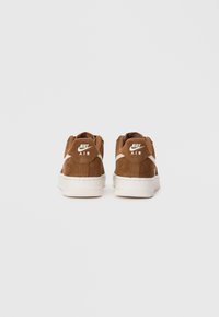 Smeđe nubuk Nike Air tenisice prikazane s leđa, s bijelim srednjim potplatima i Nike logom na potkoljenicama.