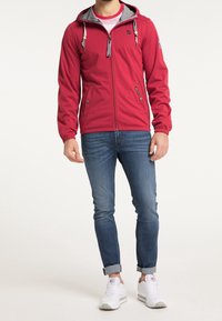 Sweat-shirt zippé rouge avec doublure grise, poignets élastiques et cordons de serrage ajustables. Associé à un jean bleu et des baskets blanches.