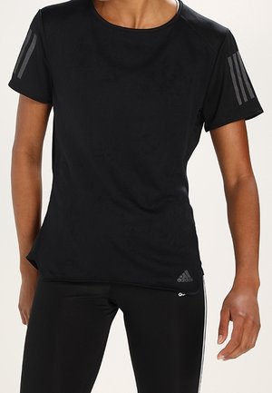 Personne portant un t-shirt noir Adidas à manches courtes avec trois bandes sur les manches et des leggings noirs avec des bandes blanches sur les côtés.