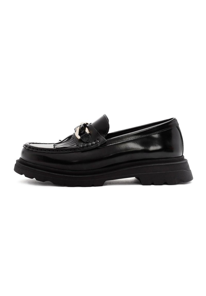 Mocasines de cuero negro con herrajes decorativos, detalles de costura y suela de goma gruesa. Textura suave con acabado brillante y forma clásica.