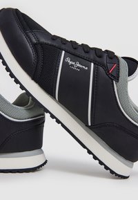 Baskets Pepe Jeans London noires et grises avec semelle blanche et adhérence texturée, inclinées pour montrer les détails latéraux et arrière.