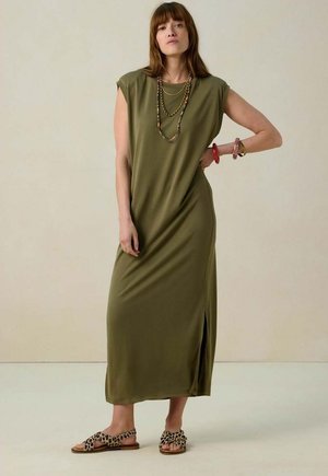 Robe maxi vert olive avec des manches courtes, présentant une fente sur le côté. Associée à des sandales à imprimé léopard et des colliers superposés. Texture lisse.