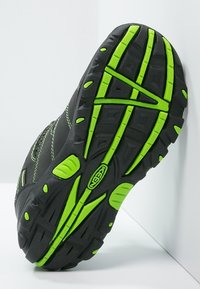 Musta kenkäpohja, jossa on elävä vihreä yksityiskohta. Sisältää teksturoitua kumipintaa pidon parantamiseksi, mukaan lukien nystyrät ja pitoalueet.