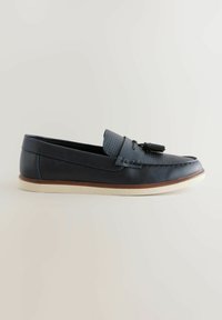 Mocasines de cuero marino con un acabado texturizado, acento de borlas y suela blanca contrastante. Interior acolchado para mayor comodidad y forma estilizada.