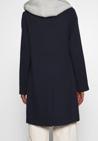 Dunkelblauer Mantel mit strukturierter Oberfläche, grauer Kapuze, langen Ärmeln und geradem Schnitt, mit einer Naht in der Mitte des Rückens und minimalen Details.