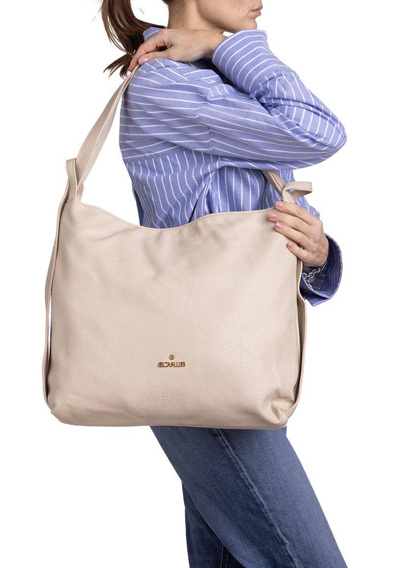 Borsa a spalla in pelle beige con una forma rilassata; presenta un logo dorato e una lunga tracolla regolabile, mostrata su uno sfondo neutro.