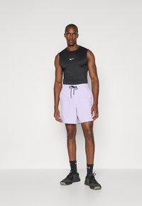 Haut sans manches Nike noir avec logo blanc, associé à un short violet clair avec taille élastique et cordon noir. Chaussures et chaussettes noires.