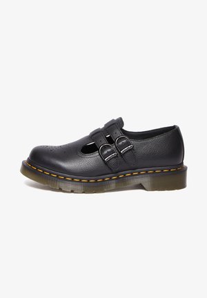 Sapato de couro preto com design perfurado, duas fivelas, sola de borracha e costura amarela ao longo da borda. Forma de bico arredondado e plano.