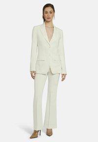 Witte op maat gemaakte kostuum met een getailleerde blazer met twee knopen en klepzakken, gecombineerd met uitlopende broeken. Glad, gestructureerd materiaal met een slanke silhouet.