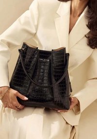 Sort håndtaske med krokodilleprægning og struktureret design, som har en enkelt rem og et brandlogo på en glat panel.