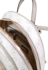 White backpack with a patterned exterior, zip closure, and silver hardware. Interior lined with beige fabric featuring a logo.