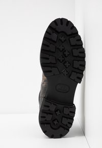 Suela negra y resistente de una bota con surcos profundos, situada verticalmente contra una pared y superficie blanca.