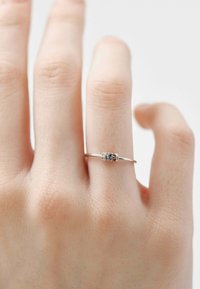 Anillo de plata en una mano con dos piedras transparentes y una azul, con un diseño de banda minimalista. Superficie suave y detalle de cierre sencillo.