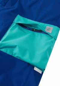 Waterproof jacket detail featuring a blue fabric with a turquoise pocket and snap closure, textured surface, and a small brand label.