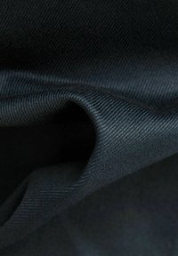 Černá tkanina s hladkou texturou a mírným leskem, vykazující zkroucený záhyb, který zdůrazňuje její pružnost a hustotu.