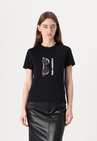 Juoda marškinėlių su grafiniu corseto dizainu ir baltu užrašu "KARL LAGERFELD". Trumpomis rankovėmis ir patogiu kirpimu.