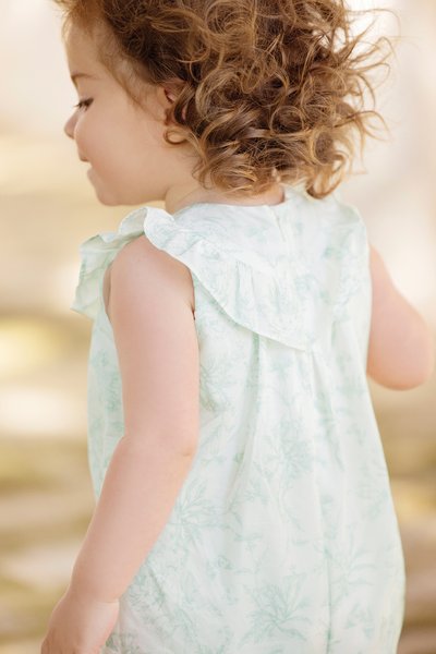 Light green, floral-patterned sleeveless dress with ruffled shoulder detail and a back button closure. Soft fabric texture, gentle design.