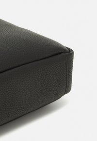 Coussin en cuir noir avec une surface texturée, possédant un bord lisse et des coins arrondis, conçu pour le confort et le soutien.