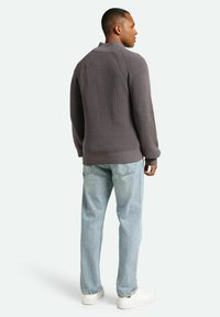 Charcoal knit sweater with a high collar, ribbed texture, and drop shoulder design, paired with light blue denim jeans and white sneakers.