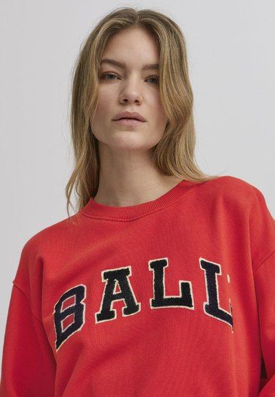 Rød genser med svart og krem brodert tekst "BALL" på brystet, med rund hals og teksturert stoff.