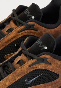 Baskets en daim marron et mesh noir avec des accents noirs, présentant une tige texturée, des lacets noirs et un logo Nike bien visible.