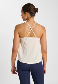 Light beige sleeveless top with crisscross straps and a slightly loose fit, made from a soft fabric, perfect for layering.