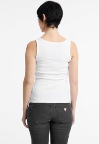 Witte, mouwloze tanktop van ribstof, gecombineerd met donkergrijze, strakke jeans met een klein logopatch op de achterzak.